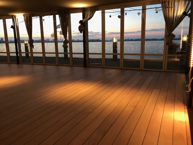 Houten vloer in ruime zaal met uitzicht op het water bij zonsondergang